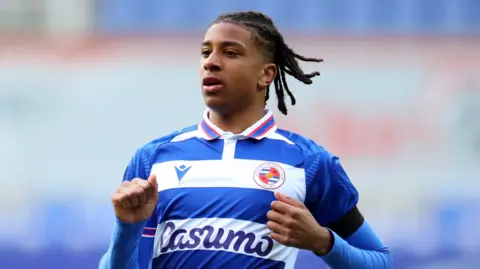 Michael Olise wearing a blue and white Reading FC shirt during a match. 