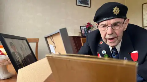 Normandy veteran Cliff Dalton looking at a picture of himself as an 18 year old soldier in World War Two