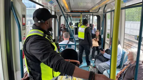 Security officers wearing high-visibility uniform on a packed tram in Nottinghamshire. 