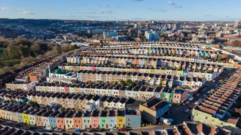 Aerial view of Bristol from the sky. You can see lines of rainbow-coloured homes, with a blue sky in the background.