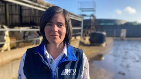 Abi Reader of NFU Cymru stands in front of cows in her farmyard.