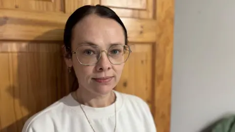 A woman with tied back brown hair and a white t shirt and glasses