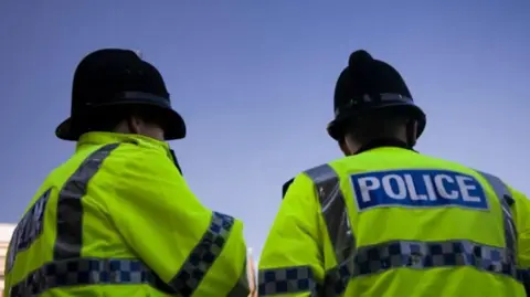 Getty Images Two police officers wearing high-visibility jackets facing away from the camera