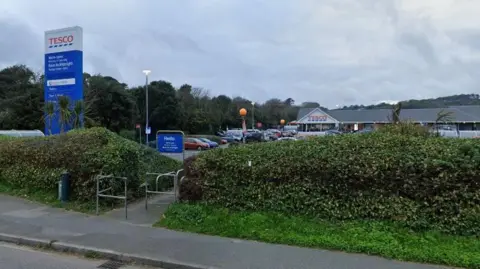 A street view image of a Tesco supermarket in Penzance. Hedges line the perimeter of the car park.