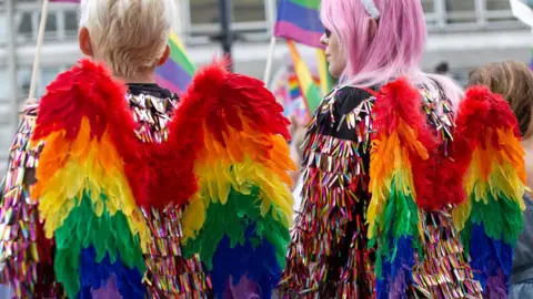 Pride parade goers with angel wings in the style of the rainbow flag, commonly known as the gay pride flag or LGBTQ pride flag
