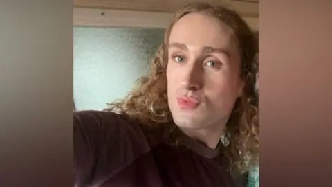 West Mercia Police A person with long curly blonde hair and a black top looks at the camera.