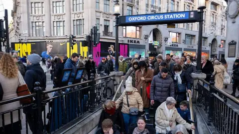Shoppers and visitors out on Oxford Street walk down the steps into a very busy Oxford Circus underground station.