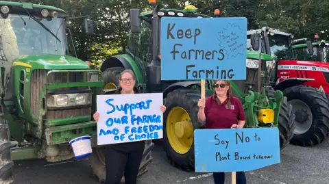 Protesters with placards standing in front of tractors at the meeting