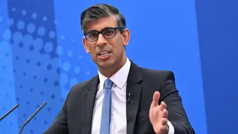 Getty Images Rishi Sunak speaking in front of a microphone in front of a blue background