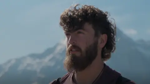 Man with beard looking out to the horizon at top of a mountain