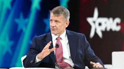 Getty Images Sits Erik Prince on a chair looking at one side and indicates his hand while speaking at a conference