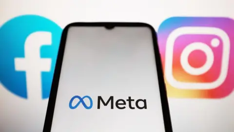 A Meta logo displayed on a smartphone screen with Facebook and Instagram logos on a computer screen in background
