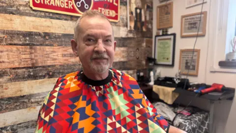 A man wearing a patterned gown, having a haircut at a barbershop.
