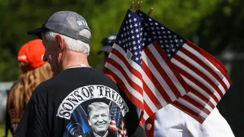 A man stands with his back to the camera holding an American flag while wearing a Trump T-shirt at a rally in Pittston on 16 July.