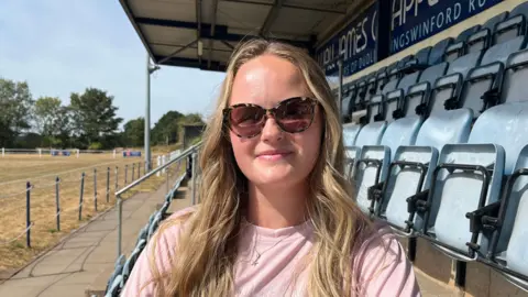 A close-up of a woman with long blonde hair sitting on a seat in a stadium.