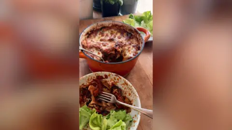 A bowl of lasagne in front of a pan of lasagna