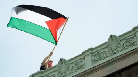 Image shows a protester waving a Palestinian flag at Columbia University