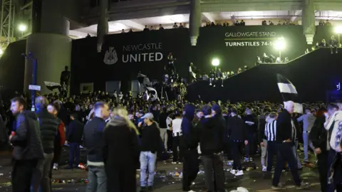 Fans outside St James' Park in the night. Lots of black of white shirts and flags and debris on the floor