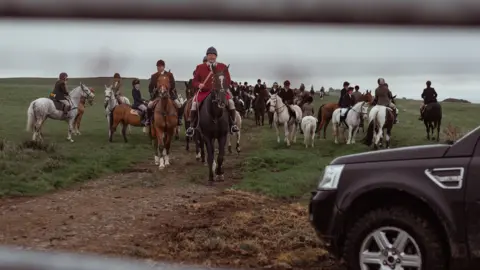 Mr John sits connected  apical  of his equine  successful  a reddish  hunting jacket. There are men connected  horses down  him successful  the tract  and a 4x4 to the close    of the image.