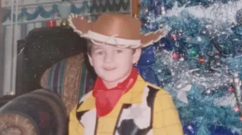 Family handout A photograph of Kaine Fletcher as a child, wearing a Woody costume, from Toy's Story', standing in front of a Christmas tree