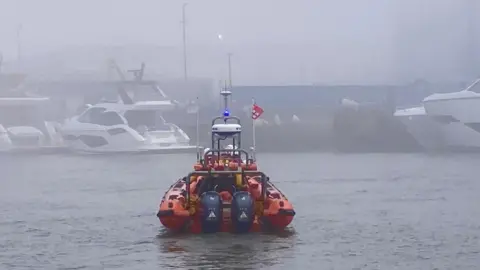RNLI lifeboat seen from the rear on the water in foggy conditions with numerous boats.