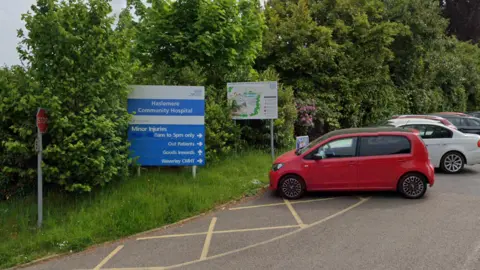 A hospital car park lined with leafy green trees.