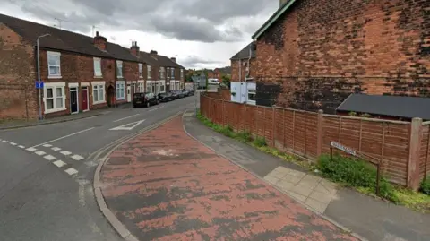 Google A road junction, with rows of terraced houses and a wide pavement that has red paint covering a section of it.