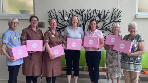 A row of woman – including nurses – holding pink Breast Friends boxes