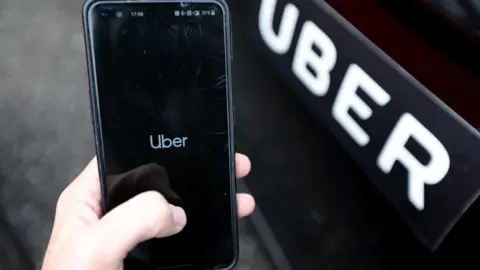 Getty Images Uber app on a phone next to an Uber branded car