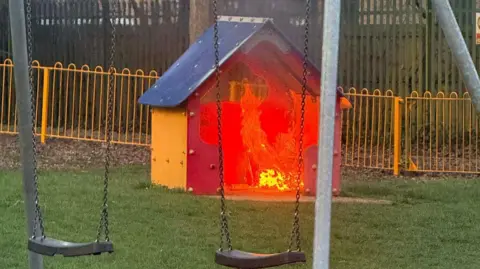 A children's play area. There is a shed on fire.