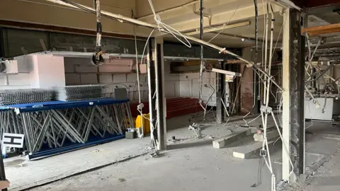 John Devine/BBC The inside of a former pub with flooring, ceiling and walls removed, lots of electrical wires hanging from what looks like steel supports vertical and horizontal.