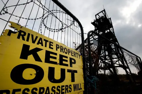 Roger Tiley Mine winding gear with a keep out sign, fencing and barbed wire in front of it