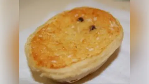 Oval-shaped cheesecake with golden brown top and puff pastry around the outside. Two currants are visible on the surface.