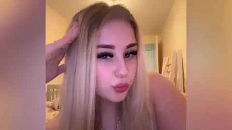 Tiffany Tiffany, is a blonde woman in her late teens. She has thick dark eyelashes and pouts in this selfie.