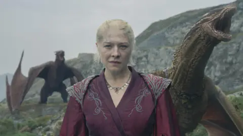 HBO Een vrouw in een rode historische jurk met rode draken naast haar en op de achtergrond