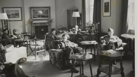 Getty Images A black and white photo of the Canadians' New Beaver Club for Canadian soldiers on leave in London, showing one of the fine lounges where the men are sat reading