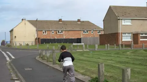 Getty Images  A child on a scooter rides on the pavement towards a council estate.