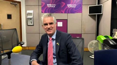 MP James Cartlidge wearing a navy suit during a visit to the BBC Radio Suffolk studio in Ipswich.