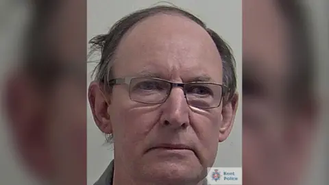 Police photo of David Fuller, he is looking slightly off camera and wearing thin-rimmed glasses. He has short dark hair.