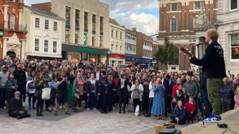 Martin Giles/BBC A crowd in Ipswich town centre watch singer-songwriter Ed Sheeran perform an impromptu gig with his guitar. 