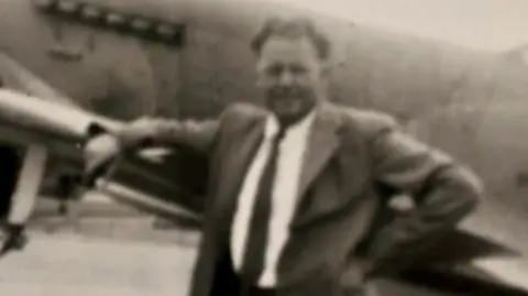 Family handout An old photograph of the father. He is wearing a suit and appears to be in front of a plane. 