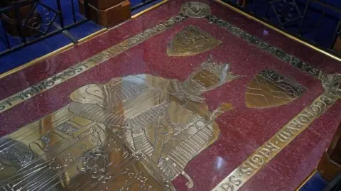 PA Media The tomb stone of Robert the Bruce with an image of the king in brass inlaid into red stone. 