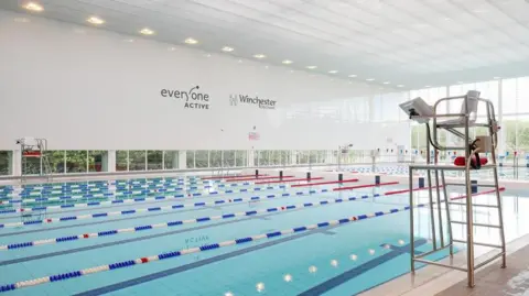 Swimming pool with lane ropes running along its length and a lifeguard seat on the near side of the pool.