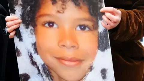 Hands holding a poster of a close up of the face of Zane Gbangbola aged seven