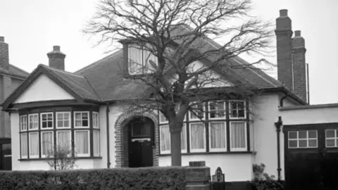 PA Media Black and white image of the bungalow in north west London which was the centre of a Soviet spy ring in the early 1960s. The bungalow has a white rendered facade and a neat hedge at the front. There is also a tree in front of it.
