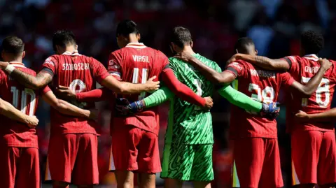 Rear view of Liverpool players from Getty Images putting their arms around each other's necks during a minute's silence