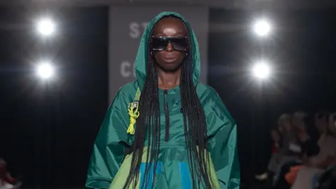 Chris Yates/Oxfam Model Eunice Olumide is pictured on the catwalk wearing sunglasses and a blue and green dress made out of recycled tents.