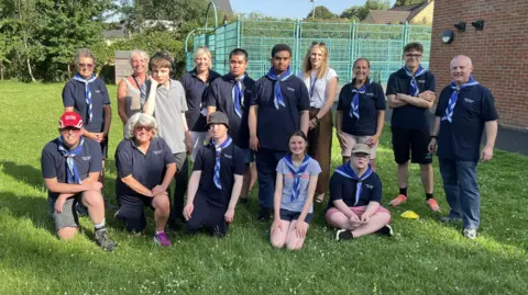 Eight teenagers pose for the camera with scout leaders and Fosse Way school headteacher