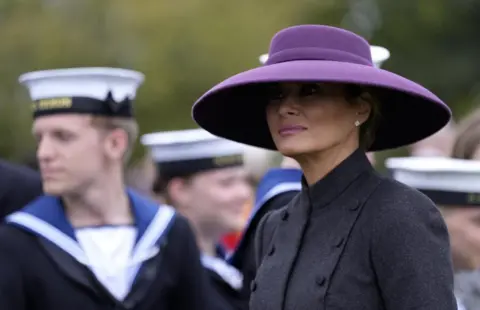 Andrew Matthews/Reuters Melania usa un abrigo gris de estilo militar y se ve con el ahora icónico sombrero morado el miércoles durante el día