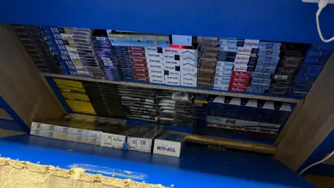 West Northamptonshire Council A wooden panel has been pulled back to reveal shelves filled with cigarette packets. 
